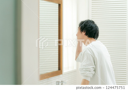 Young man looking in the mirror and taking care of his skin Young man looking in the mirror and taking care of his skin 124475751