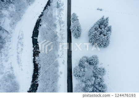 Winter road near mountain river in snowy scenery, drone aerial view 124476193