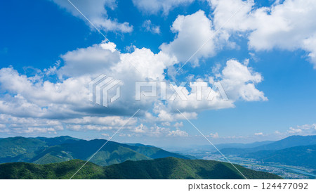 藍天上有許多白雲，山巒被綠色植物包裹著 124477092
