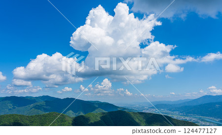 藍天上有許多白雲，山巒被綠色植物包裹著 124477127