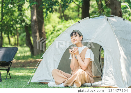A girl drinking a drink in front of a tent at a campsite or leisure facility 124477394