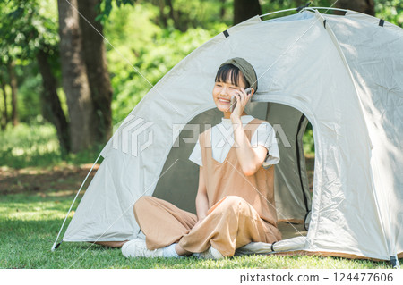 A girl talking on a smartphone in front of a tent at a campsite A girl talking on a smartphone in front of a tent at a campsite 124477606