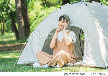 A girl talking on a smartphone in front of a tent at a campsite 124477607