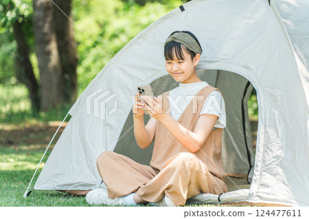 A girl looking at her smartphone in front of a tent at a campsite 124477611