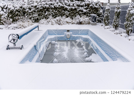 Snow-covered outdoor swimming pool in a winter backyard. The frozen water and snowy surroundings create a tranquil, cold-weather atmosphere. Snow-covered outdoor swimming pool in a winter backyard. The frozen water and snowy surroundings create a tranquil, cold-weather atmosphere. 124479224