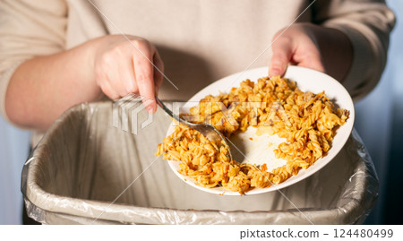 Woman throwing away food leftovers into garbage bin trash. Scraping food with spoon. Compost from leftover food. Environmentally responsible, reducing pollution. 124480499