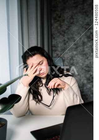 Woman working from home office sitting with laptop rubbing tired eyes. Burnout, stress, fatigue at work concept 124480508