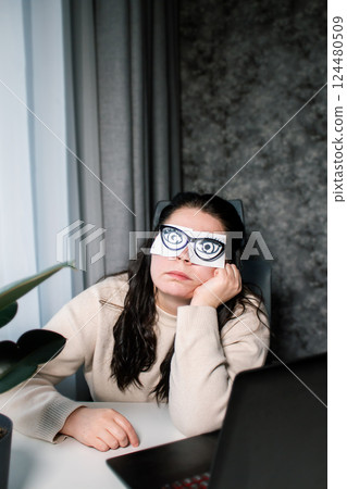 Tired Caucasian woman freelancer feeling stressed from work problems. Irritation burnout. Painted eyes on adhesive notes glued to face. Not having enough sleep 124480509