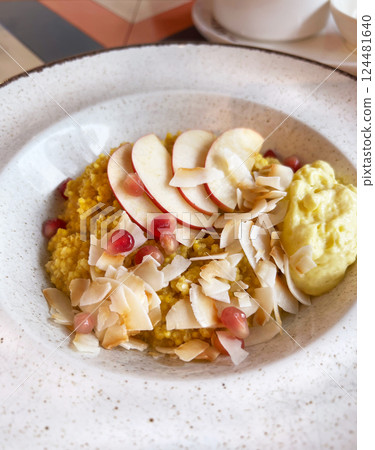 Nutritious millet porridge topped with fresh apple slices, pomegranate seeds, and coconut flakes, served with a creamy side. An appealing and healthy gluten free breakfast option Nutritious millet porridge topped with fresh apple slices, pomegranate seeds, and coconut flakes, served with a creamy side. An appealing and healthy gluten free breakfast option 124481640