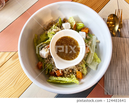 Fresh quinoa salad served in white bowl with lettuce, feta cheese, roasted pumpkin, nuts, flavorful dressing in separate dish on wooden table , healthy gluten free plant based breakfast option Fresh quinoa salad served in white bowl with lettuce, feta cheese, roasted pumpkin, nuts, flavorful dressing in separate dish on wooden table , healthy gluten free plant based breakfast option 124481641