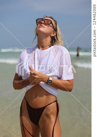 A woman in a white shirt and sunglasses is on the beach A woman in a white shirt and sunglasses is on the beach 124482089