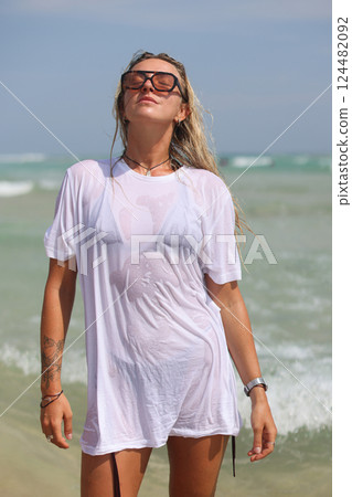 A woman in a white shirt and sunglasses is on the beach 124482092