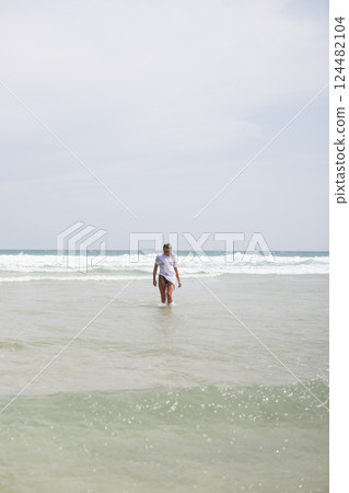 A woman is confidently walking out of the vast ocean onto the beach 124482104