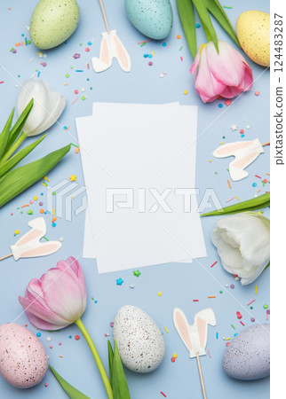 Easter eggs and tulips framing blank greeting card on pastel blue background Easter eggs and tulips framing blank greeting card on pastel blue background 124483287