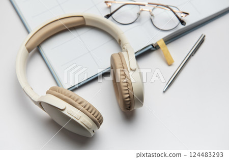 Wireless headphones, planner, eyeglasses and pen lying on white table Wireless headphones, planner, eyeglasses and pen lying on white table 124483293