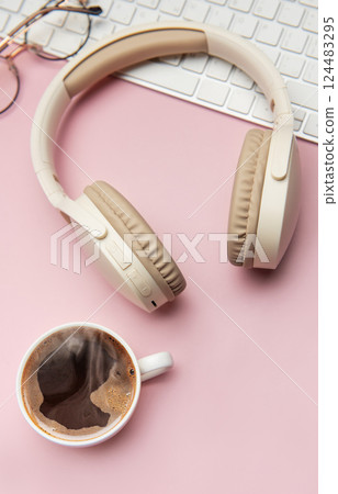 Coffee break accessories on pink table, headphones, keyboard and glasses 124483295