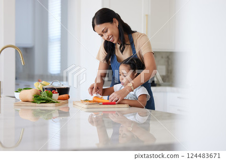 Cooking food, mother and child cutting vegetables helping prepare healthy vegan diet dinner in the kitchen at home learning and having fun. Happy woman and girl kid family teaching culinary skills 124483671