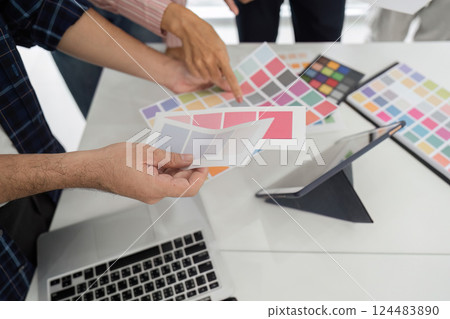 Collaboration and Creative Review. Diverse team discussing color palettes and design elements in a modern workspace. 124483890