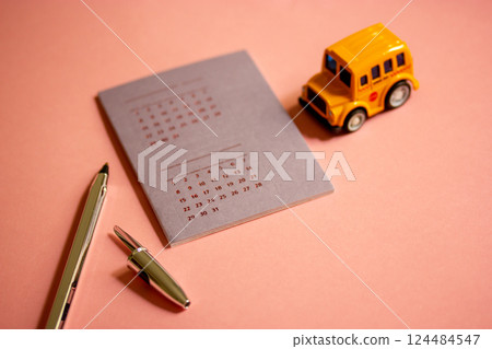 Toy yellow American school bus, calendar with dates, golden pen on pink table. Stationery for studying and planning. Back to school Supplies for study 124484547