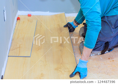Carpenter is carefully laying laminate flooring in partially renovated room, on precise placement. 124487396