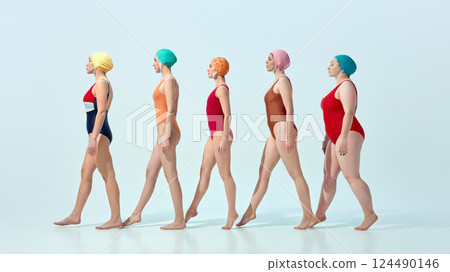 Women in vintage swimsuits and swim caps walking in line in rhythmical motion over light blue background 124490146