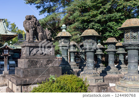 Guardian komainu lion stands on a pedestal among bronze lanterns 124490768