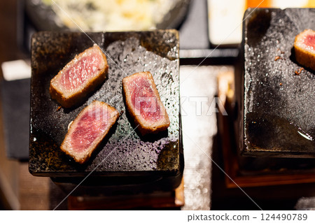 Slices of gyukatsu beef sizzling on a hot stone grill with visible marbling and crispy golden crust Slices of gyukatsu beef sizzling on a hot stone grill with visible marbling and crispy golden crust 124490789