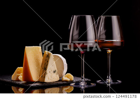 A refined selection of aged cheeses presented on a board, accompanied by a glasses of wine 124491178