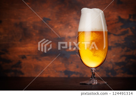 A tall glass of beer with a golden hue and frothy head A tall glass of beer with a golden hue and frothy head 124491314