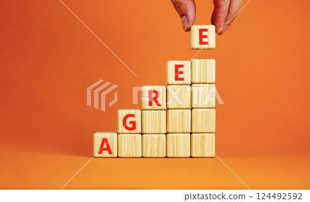 Agree symbol. Concept word Agree on beautiful wooden blocks. Beautiful orange table orange background. Businessman hand. Business agree concept. Copy space. Agree symbol. Concept word Agree on beautiful wooden blocks. Beautiful orange table orange background. Businessman hand. Business agree concept. Copy space. 124492592