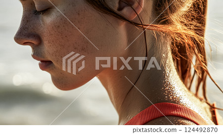 Young woman or girl with clear freckled skin in warm morning sunlight on sea beach. Female portrait in profile on the street. People workout outdoors. This is AI-generated item 124492870