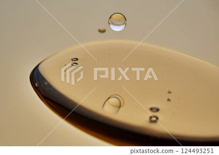 Texture of cosmetic oil with falling drop on golden background. 124493251