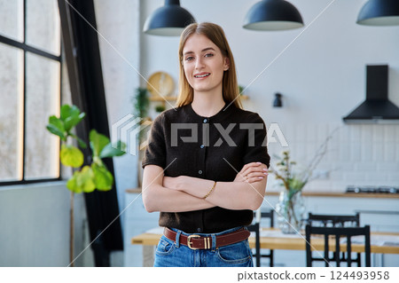 Portrait of smiling female teenager looking at camera with crossed arms in home Portrait of smiling female teenager looking at camera with crossed arms in home 124493958