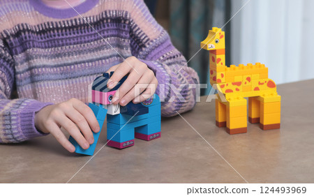 Girl plays with constructor at home on table. African animals. Children and educational games. Girl plays with constructor at home on table. African animals. Children and educational games. 124493969