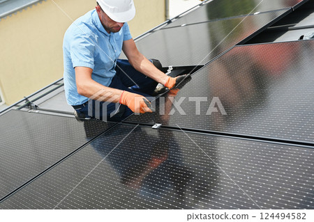 Worker building photovoltaic solar panel system on rooftop of house. Man engineer in gloves installing solar module with help of hex key outdoors. Alternative and renewable energy generation concept. 124494582