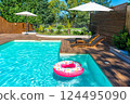 Backyard swimming pool with turquoise water, wooden deck, umbrellas, lounge chairs, and pink donut float 124495090