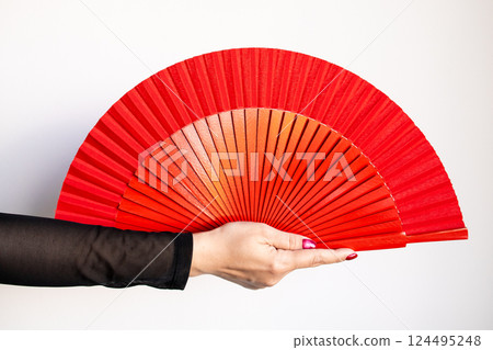 Caucasian female hand holding large red fan against white background 124495248
