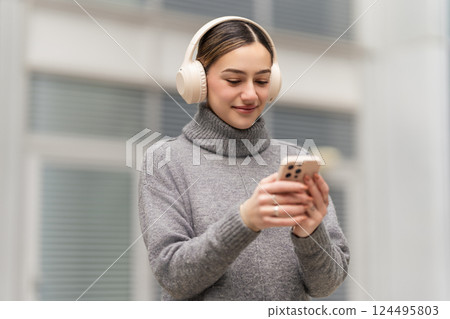 Tune in, zone out, recharge. A relaxed woman enjoys music or a podcast on her phone with headphones, finding a peaceful escape into sound while blending technology with well-being 124495803