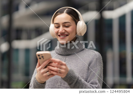 Scrolling, sharing, staying connected. A woman with headphones and smartphone reacts to social media updates, capturing real-time engagement in a world driven by digital connections 124495804