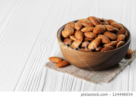 Shelled almonds are overflowing wooden bowl placed on small cloth napkin on white table, creating warm and inviting scene perfect for healthy snacking Shelled almonds are overflowing wooden bowl placed on small cloth napkin on white table, creating warm and inviting scene perfect for healthy snacking 124496034
