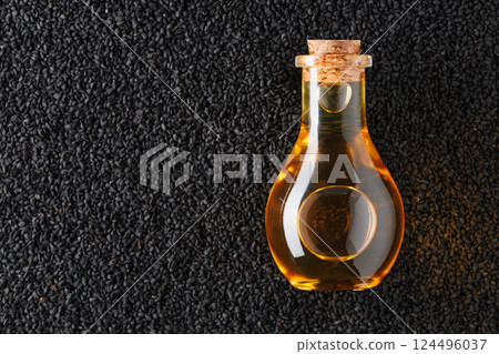 Glass bottle containing golden oil resting on bed of black cumin seeds, highlighting the rich color contrast and natural origin Glass bottle containing golden oil resting on bed of black cumin seeds, highlighting the rich color contrast and natural origin 124496037