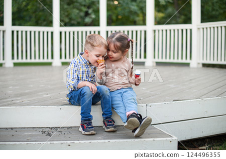 Happy Children Eating Ice Cream Outdoors on a Wooden Terrace 124496355