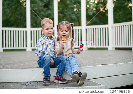 Happy Children Eating Ice Cream Outdoors on a Wooden Terrace 124496356