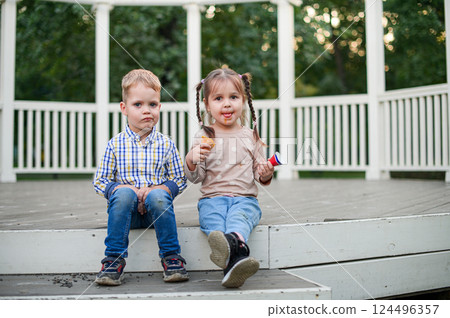 Happy Children Eating Ice Cream Outdoors on a Wooden Terrace Happy Children Eating Ice Cream Outdoors on a Wooden Terrace 124496357