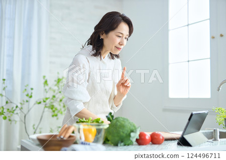 一位中年婦女一邊做飯,一邊查看平板電腦上的食譜 一位中年婦女一邊做飯,一邊查看平板電腦上的食譜 124496711
