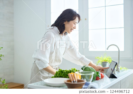 一位中年婦女一邊做飯,一邊查看平板電腦上的食譜 一位中年婦女一邊做飯,一邊查看平板電腦上的食譜 124496712