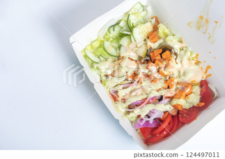 Freshly prepared salad with dressing in a takeout container on a white background. 124497011