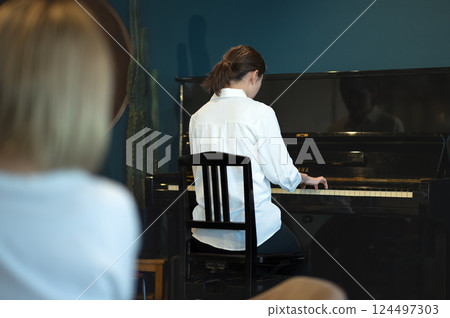 一位女士正在彈鋼琴,另一位年輕女子正在聽演奏的背影 一位女士正在彈鋼琴,另一位年輕女子正在聽演奏的背影 124497303