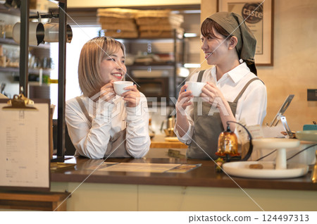 Two female baristas having a conversation while drinking coffee at the counter 124497313