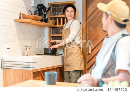 A husband talking to his wife who is cooking in a mini kitchen during a family trip to a cottage 124497510